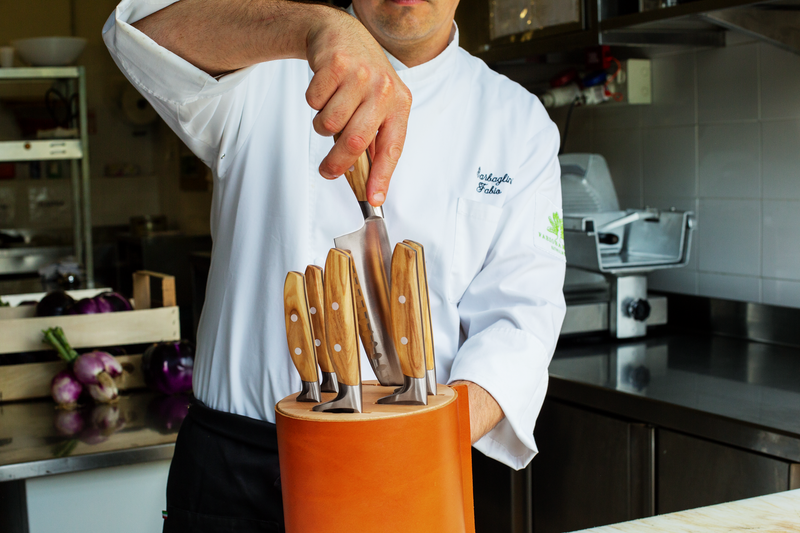 Villa 6-Slot Knife Block in tan leather with wooden-handled knives, shown with a chef removing a chef’s knife in a professional kitchen setting.