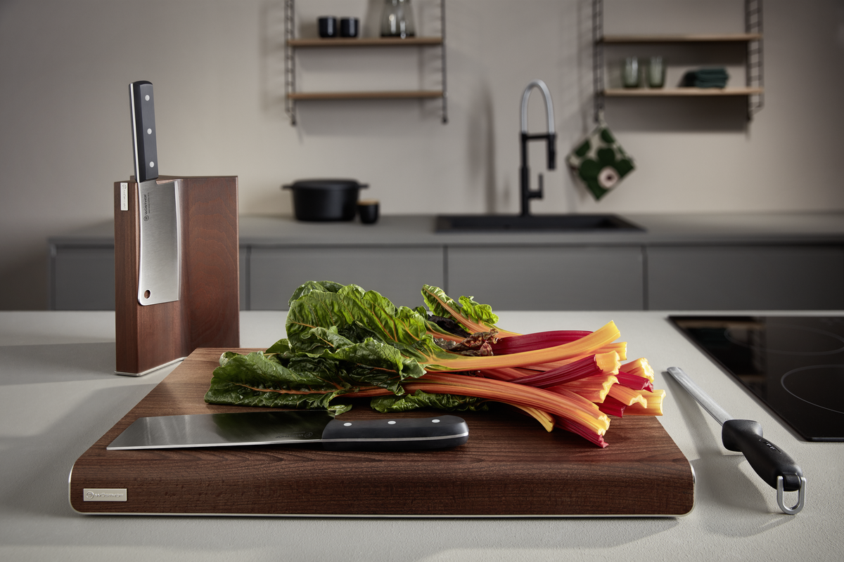 7" Chinese Chef's Knife with a sharp forged stainless steel blade and ergonomic black handle resting on a wooden cutting board with fresh greens.