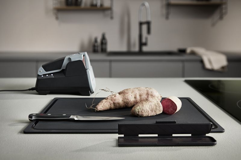 Narrow Magnetic Blade Guard in black protecting a forged kitchen knife blade on a modern kitchen countertop with root vegetables nearby.