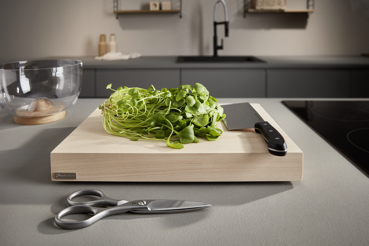 8" Chinese Chef's Knife with a sharp forged blade and a triple-riveted handle resting on a wooden cutting board with fresh greens in a modern kitchen setting.