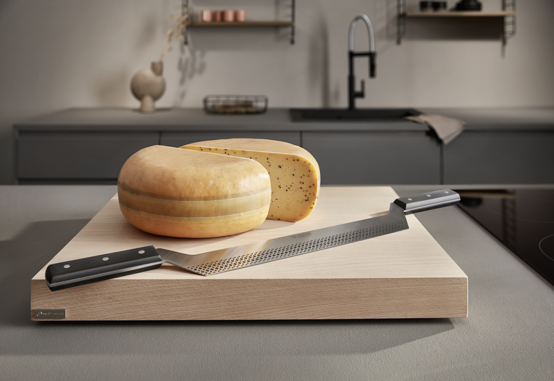 Beech Cutting Board in light wood with smooth surface holding a long WÜSTHOF forged chef's knife and two wheels of cheese in a modern kitchen setting.