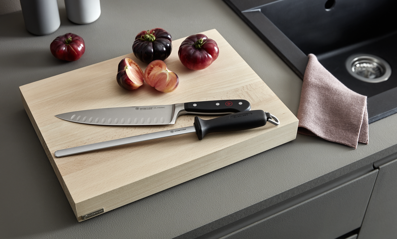 10" Diamond Sharpening Steel, Wide, Fine with black ergonomic handle placed on a wooden cutting board alongside a hollow-edge chef’s knife and heirloom tomatoes in a kitchen setting.